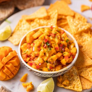fresh and juicy mango salsa served with nacho chips and other accompaniments in a white bowl