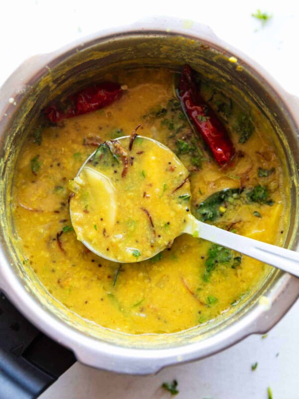 raw mango dal garnished with coriander and red chillies dal in a pressure cooker with a ladle
