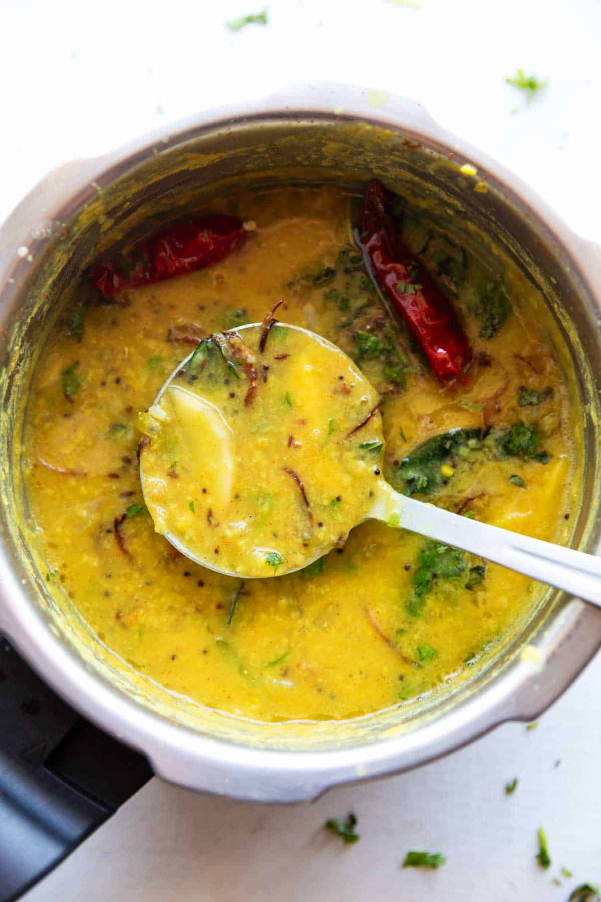 raw mango dal garnished with coriander and red chillies dal in a pressure cooker with a ladle 