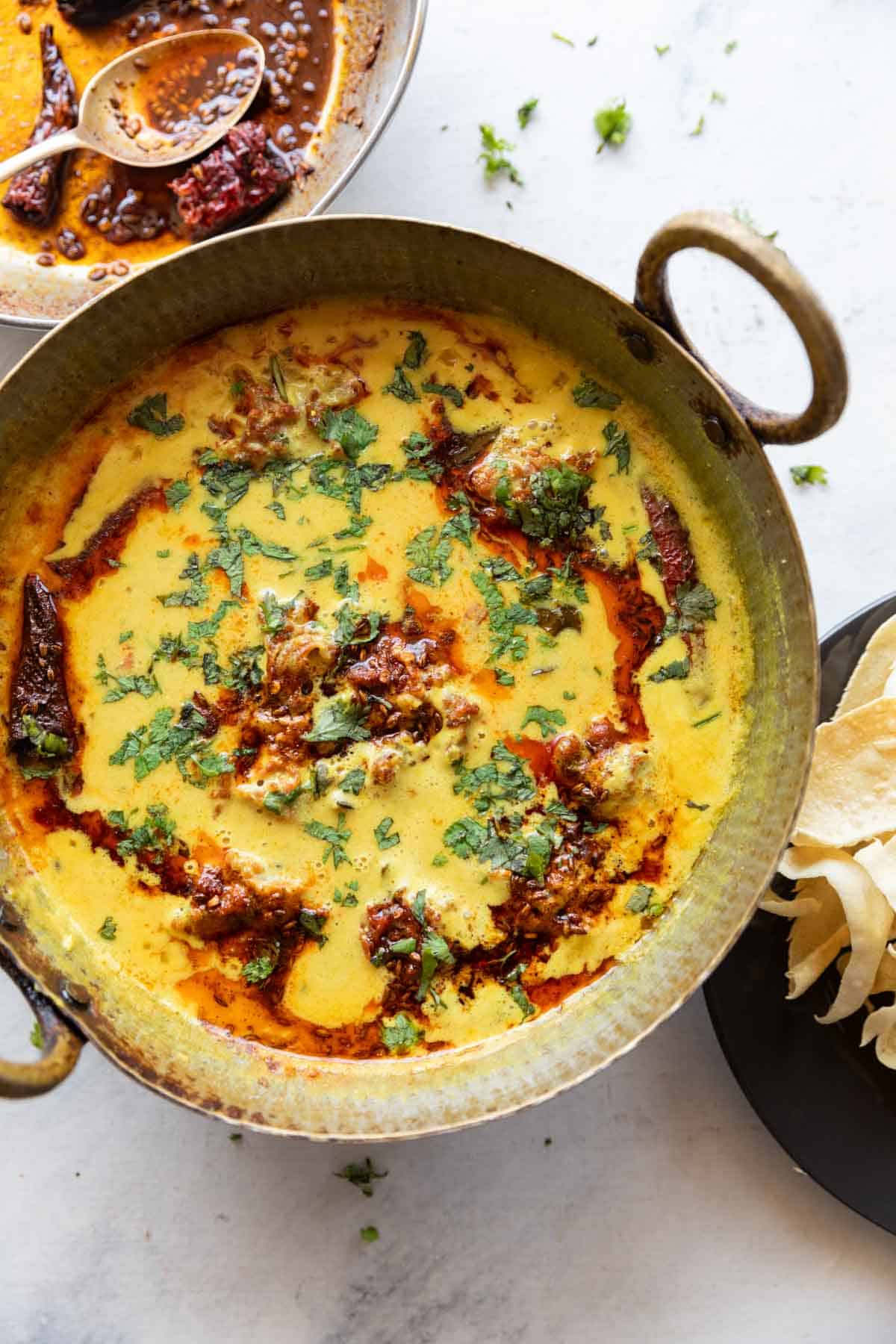 vibrant kadhi pakora garnished with a tadka and coriander leaves, served in a copper handi