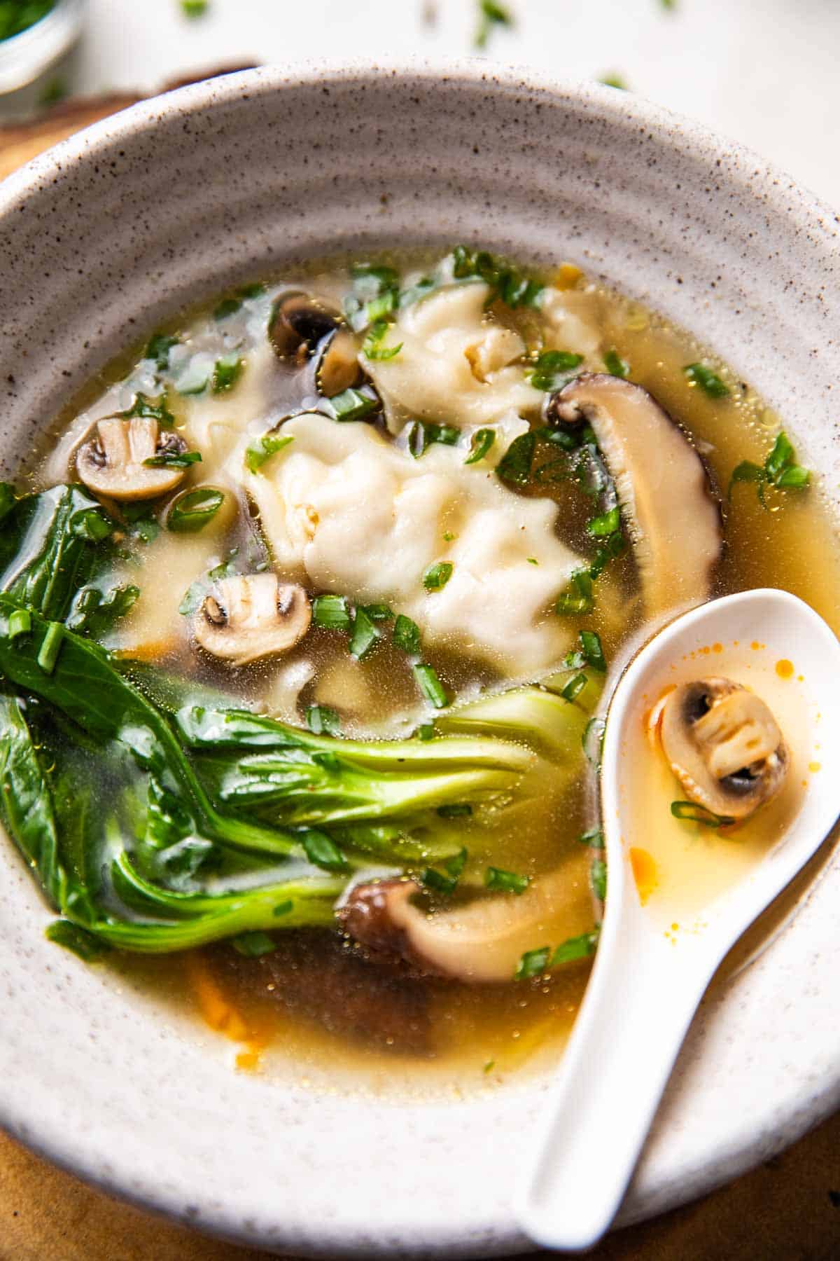 Wanton soup served in a white bowl with spoon