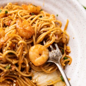 close up of chilli garlic prawn noodles served in a white bowl with a fork