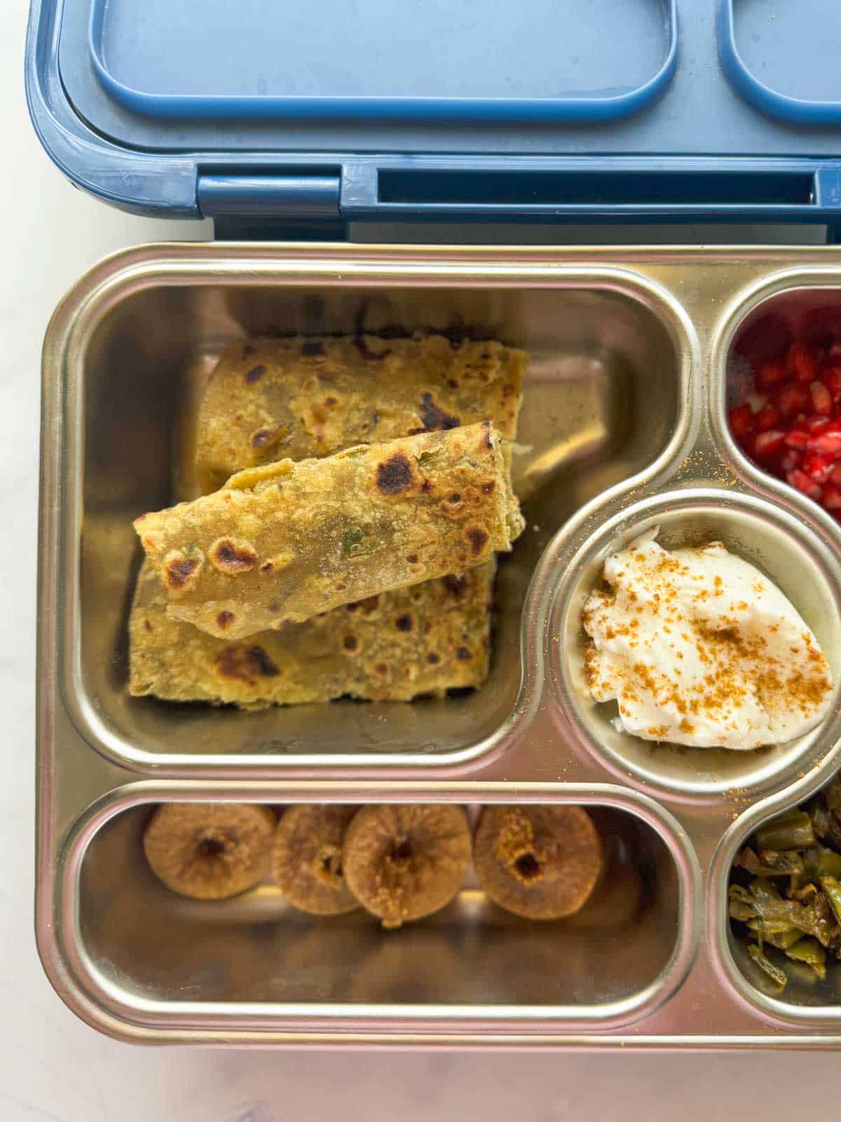 Dal paratha served in a kids tiffin box with fruits, nuts, curd and veggies