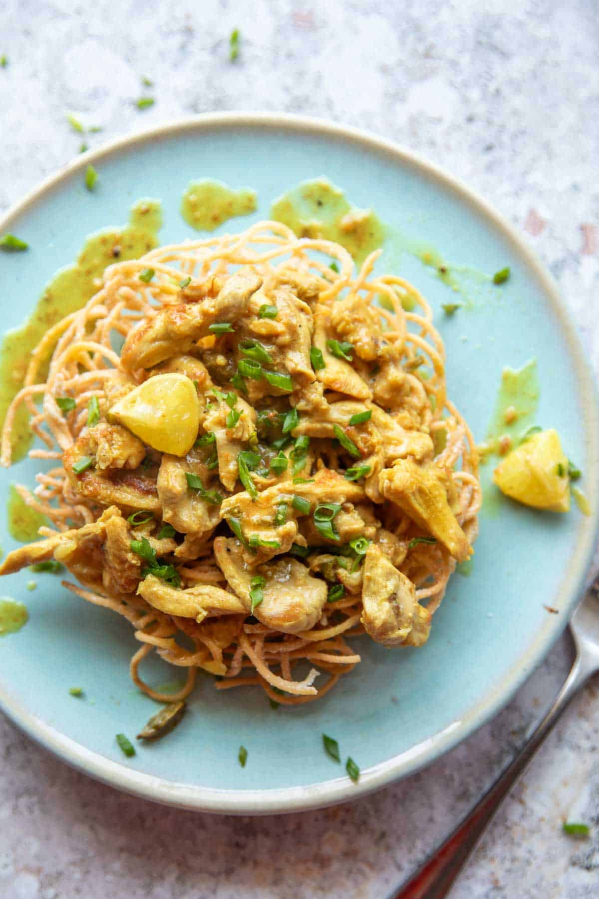 lemon chicken served on a bed of fried noodles on a blue plate with fork