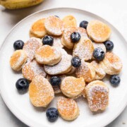 mini banana pancake bites garnished with powdered sugar & blueberries served on a white plate