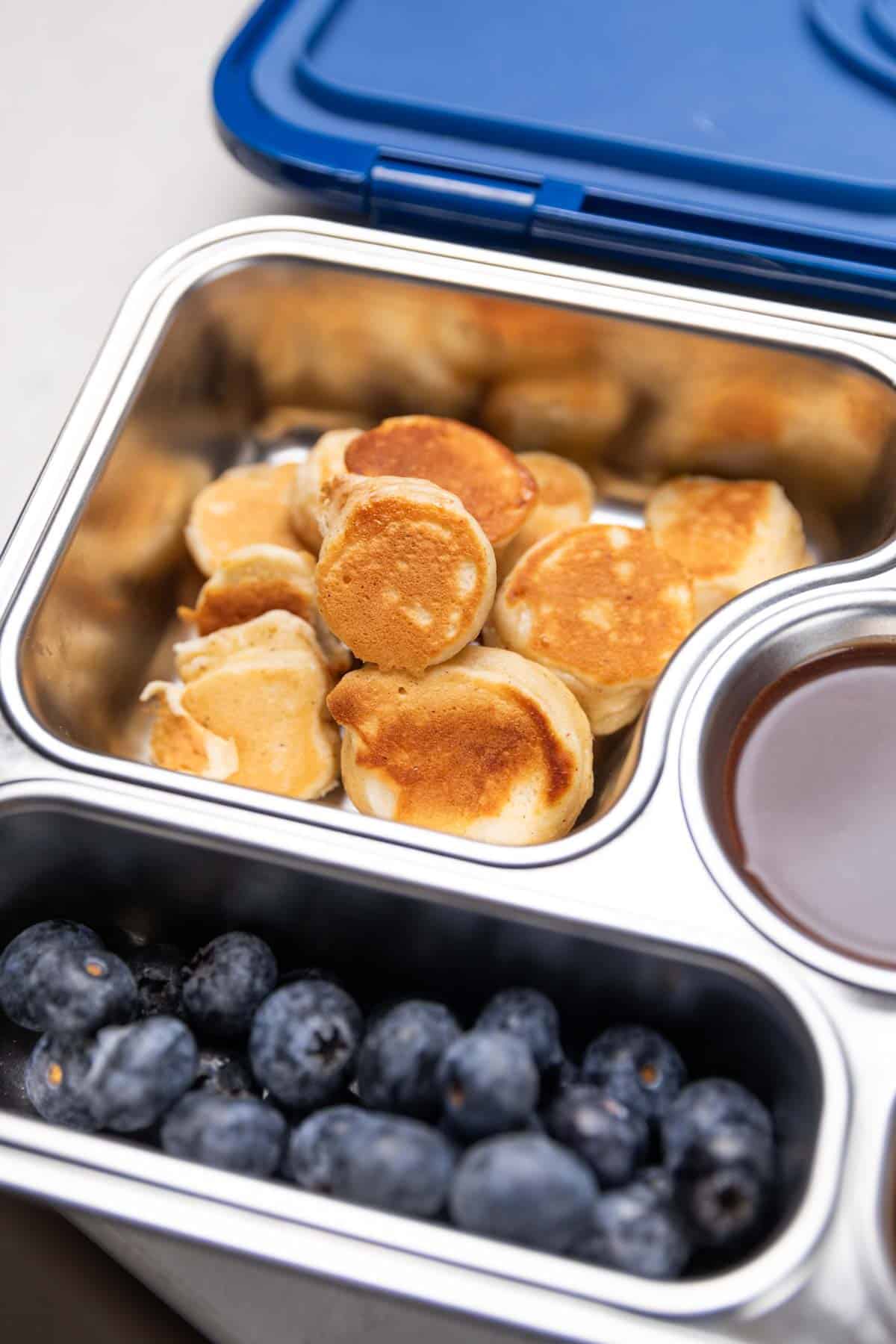 mini banana pancake bites in a tiffin box with honey and blueberries
