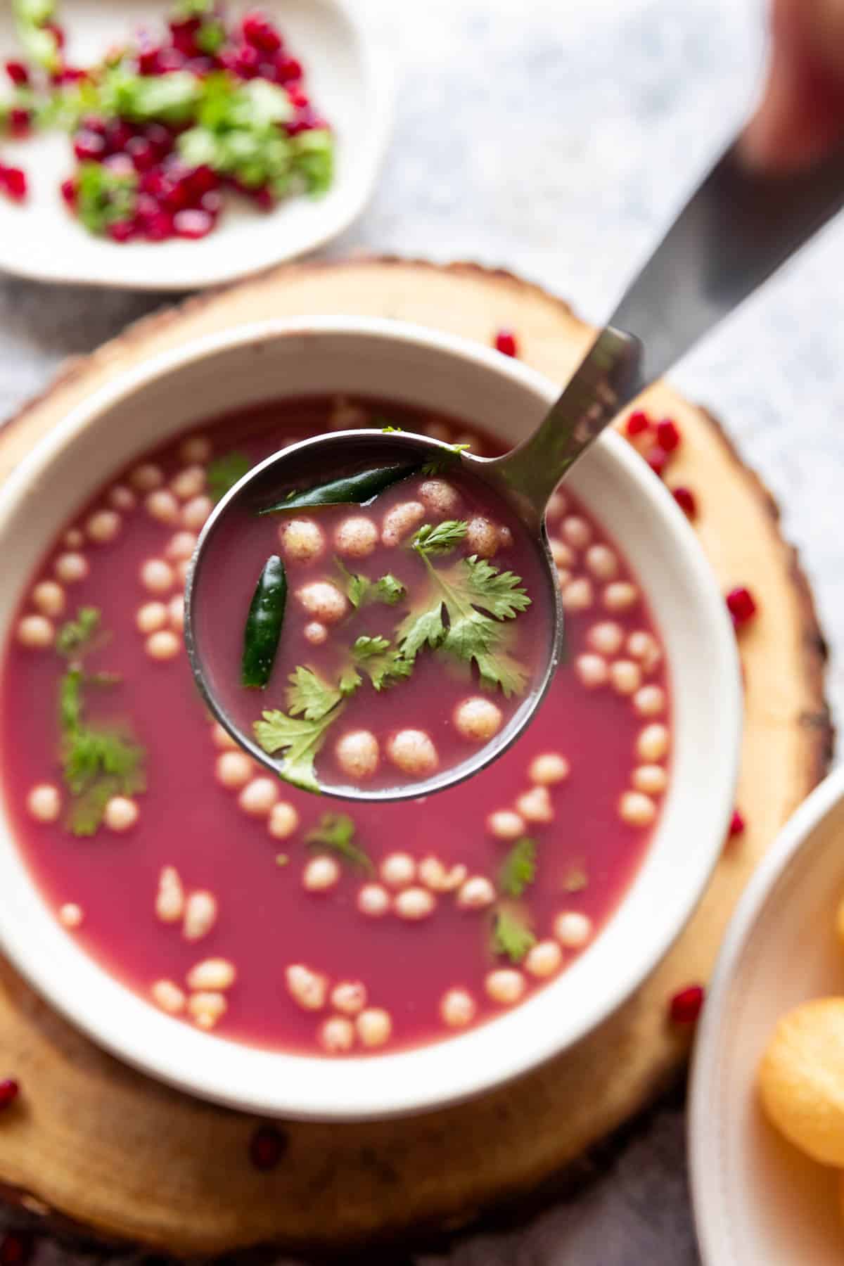 anar pani puri garnished with coriander leaves and boondi and served in a white bowl with ladle