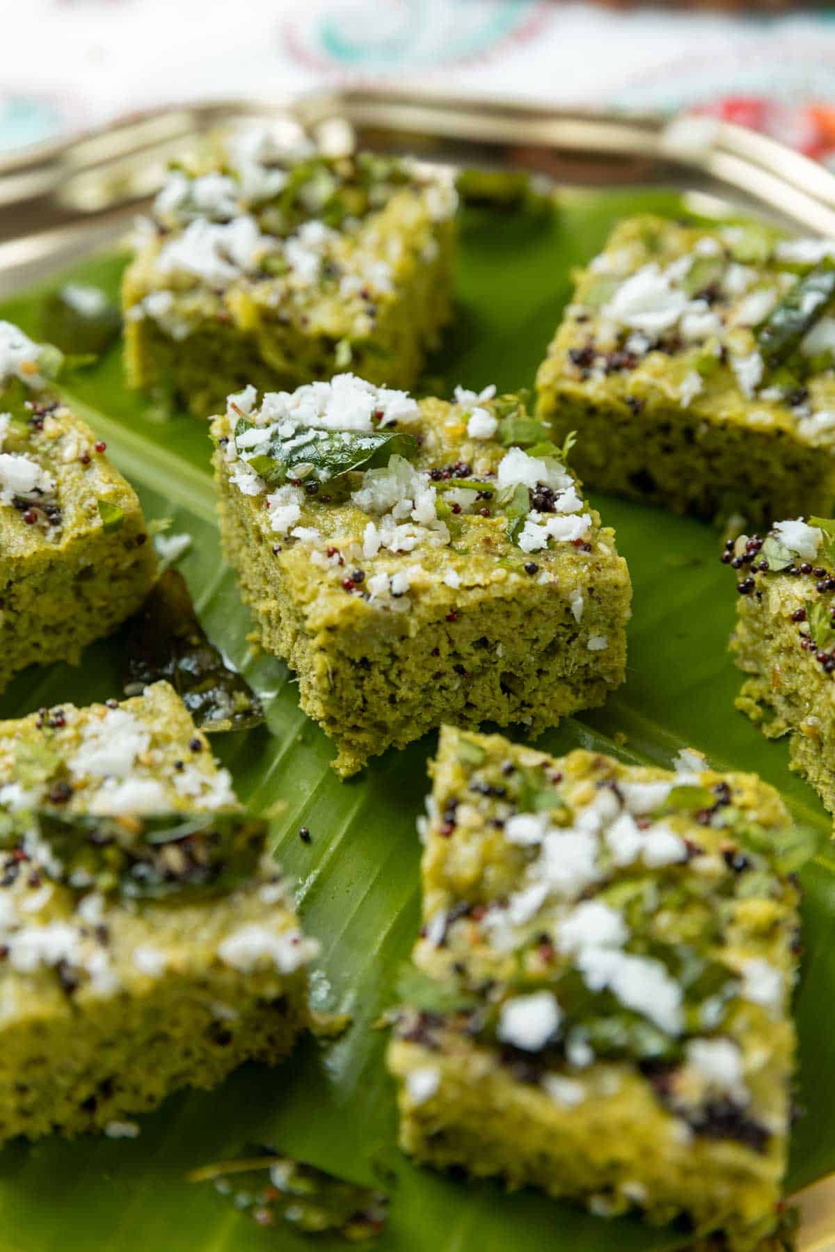 close up of sprouts dhokla garnished with tempering and served on a leaf platter