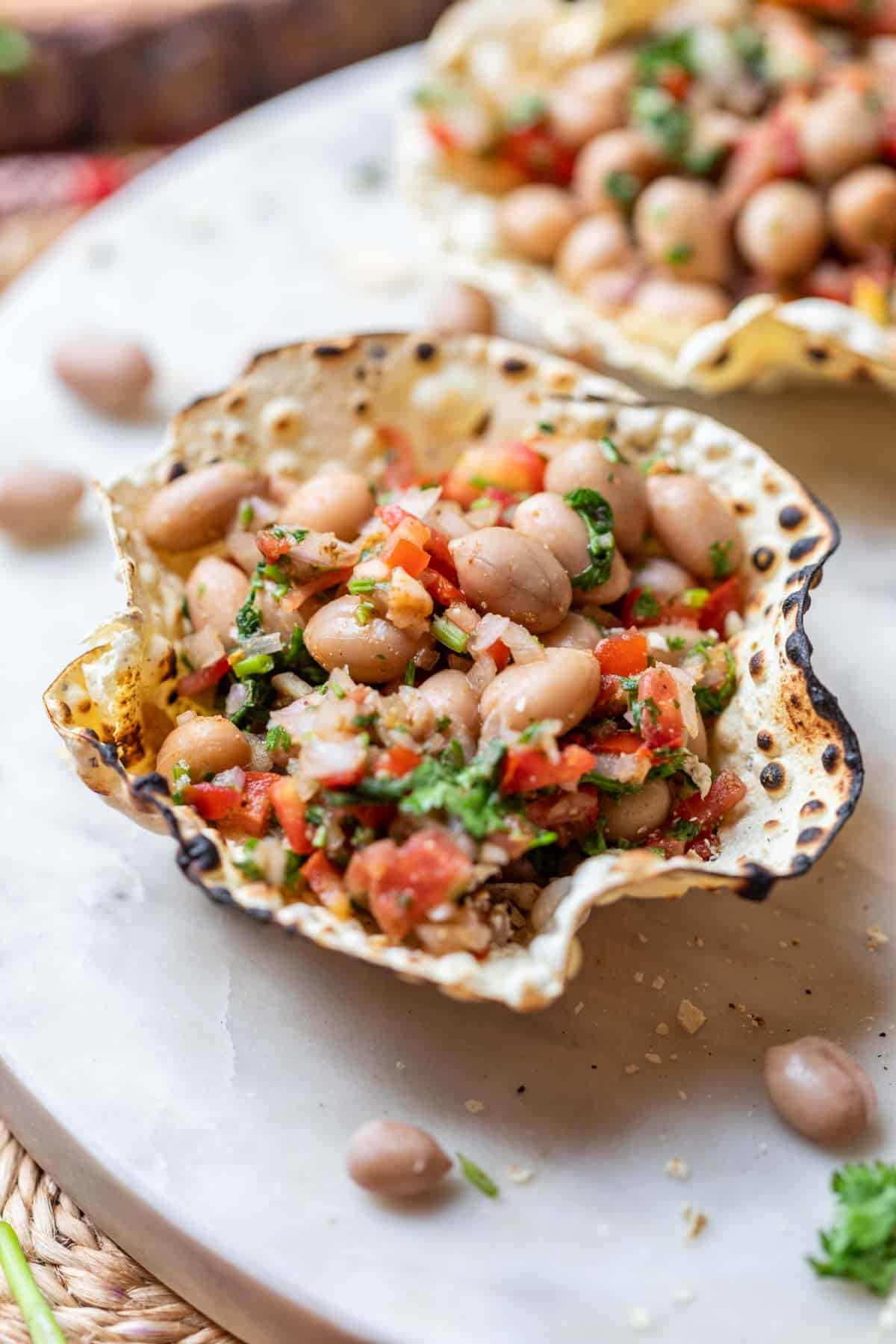 close up of edible papad bowls filled with peanut chaat and served on a white platter