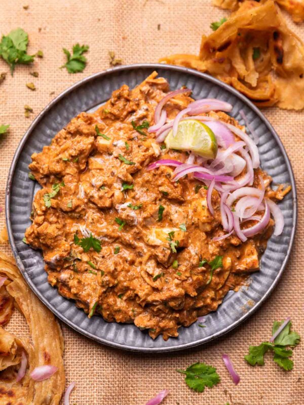 an image of chicken bharta served with sliced onion and lemon wedges