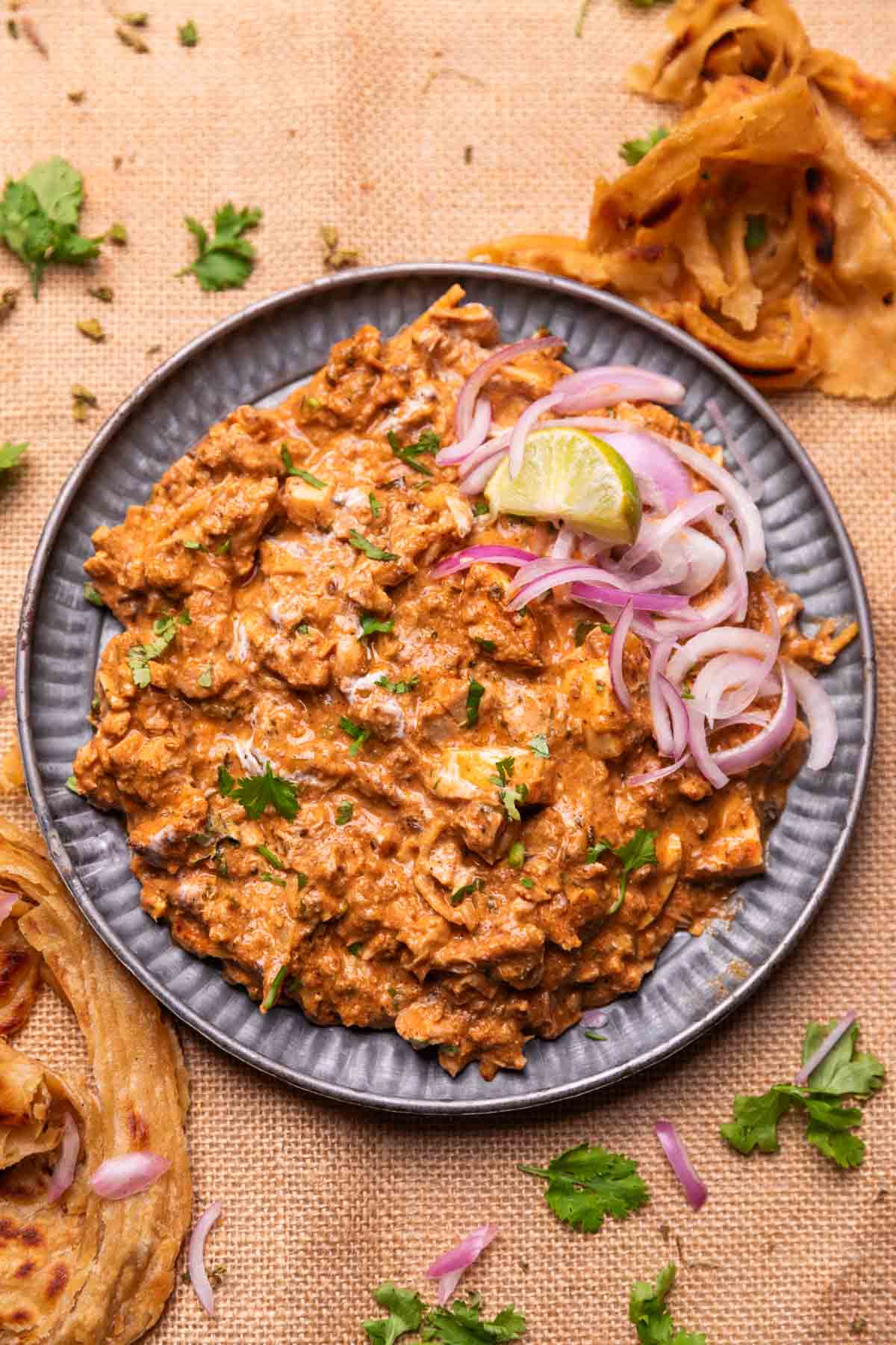 an image of chicken bharta served with sliced onion and lemon wedges