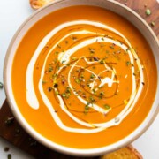 an image of roasted pumpkin pepper soup garnished with cream and pistachios along with buttered crusty bread