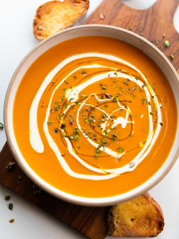 an image of roasted pumpkin pepper soup garnished with cream and pistachios along with buttered crusty bread