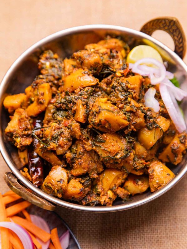 dhaba style aloo palak served in a bowl with sliced onions and a lemon wedge