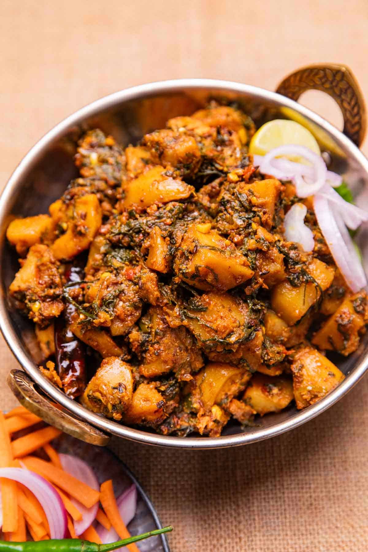 dhaba style aloo palak served in a bowl with sliced onions and a lemon wedge 