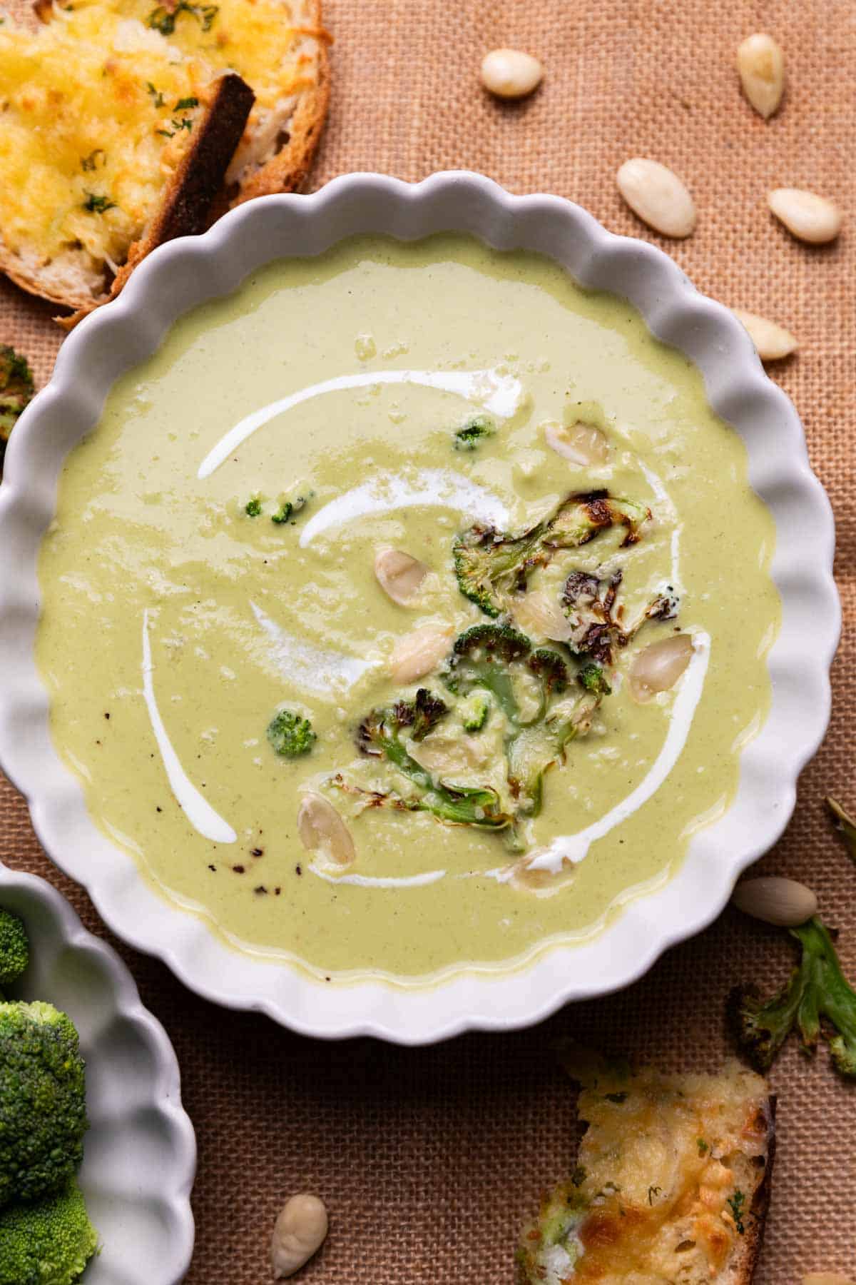 broccoli almond soup served in a white bowl with accompaniments 