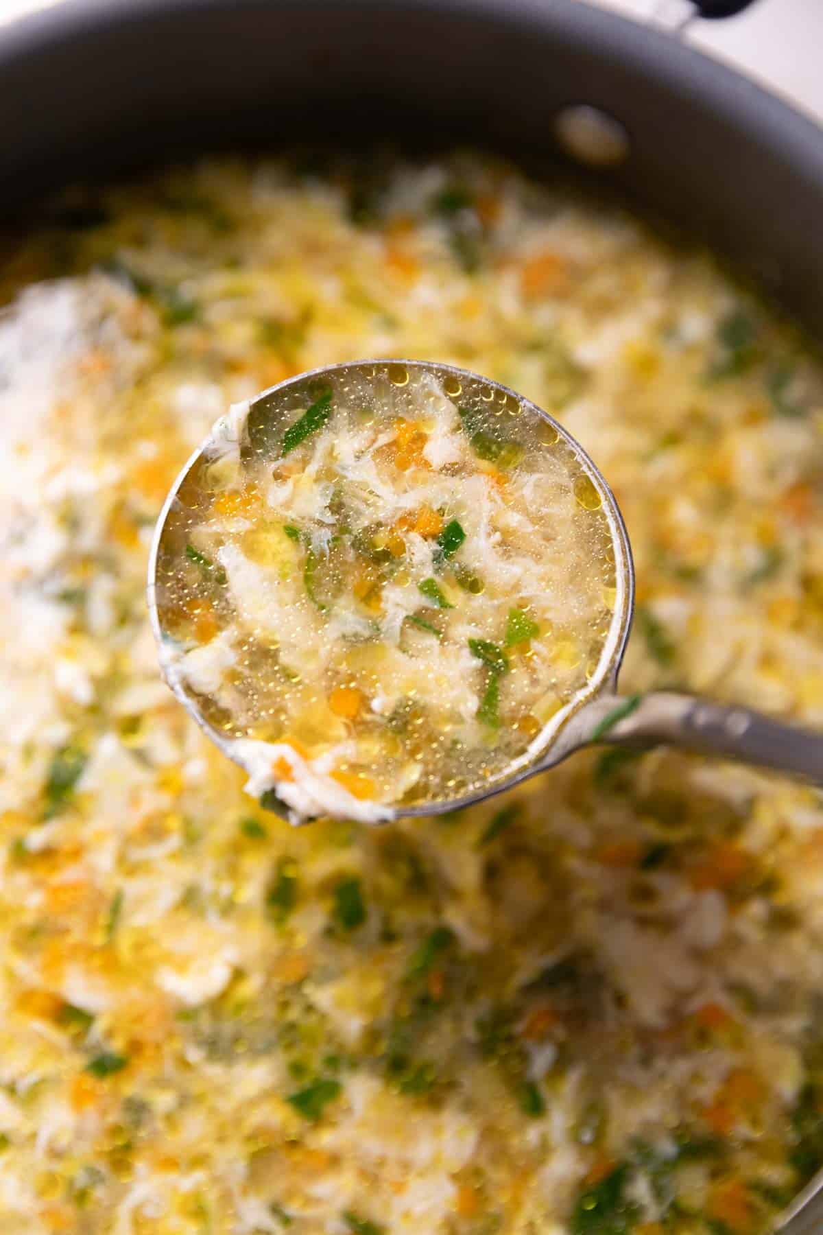 egg drop soup scooped up in a ladle to show its texture