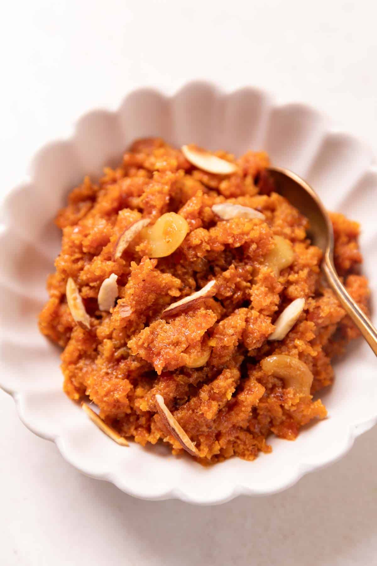 Gajar ka halwa served in a white bowl with almonds on top and a spoon on the side