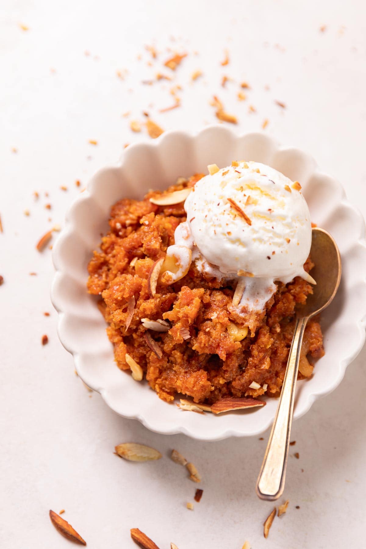 Gajar ka halwa served in a white bowl with ice cream and almonds on top and a spoon on the side
