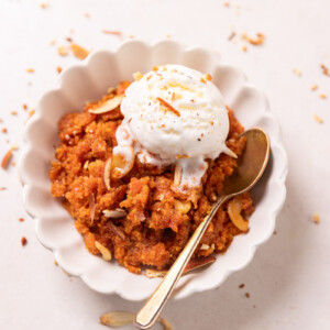 Gajar ka halwa served in a white bowl with ice cream and almonds on top and a spoon on the side