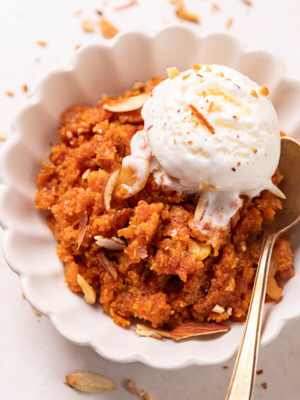 Gajar ka halwa served in a white bowl with ice cream and almonds on top and a spoon on the side
