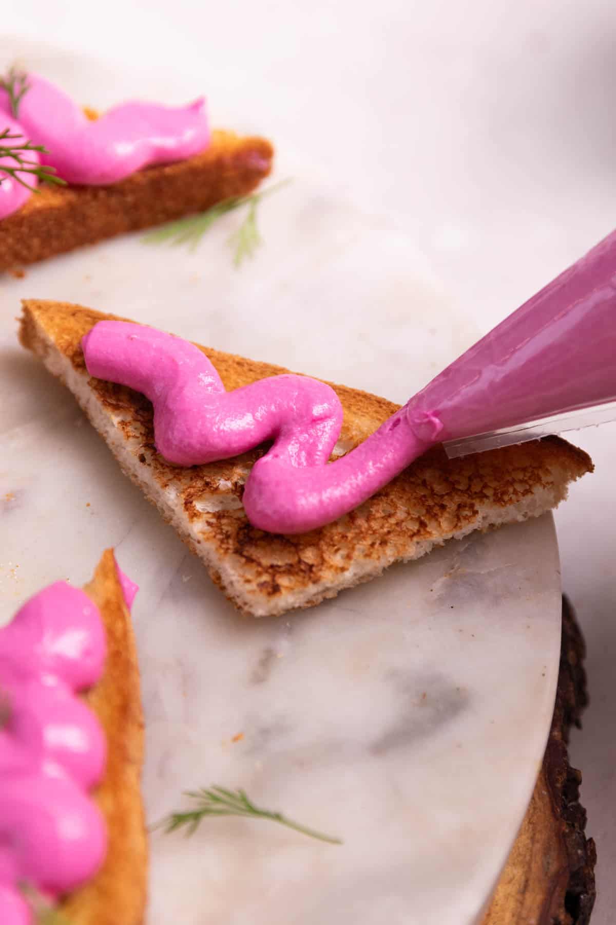 a close up image of the act of pipping paneer beetroot mix on crispy toast to show their creamy and crunchy textures