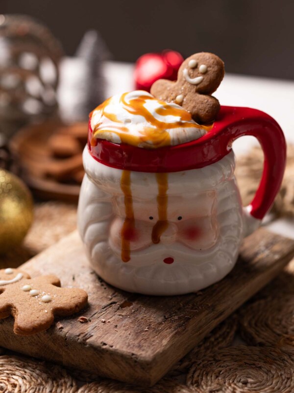 salted caramel hot chocolate served in a Santa mug and topped with whipped cream, caramel sauce and a gingerbread cookie