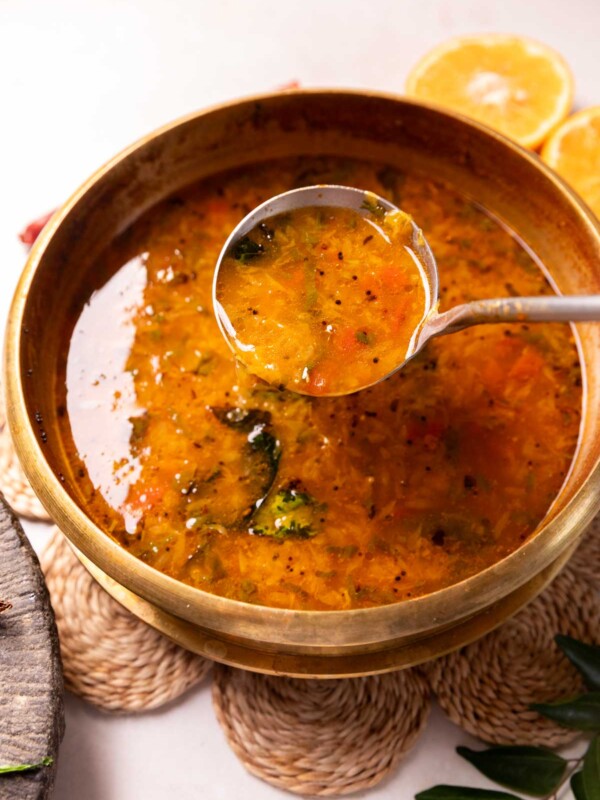 orange rasam in a container with a ladle