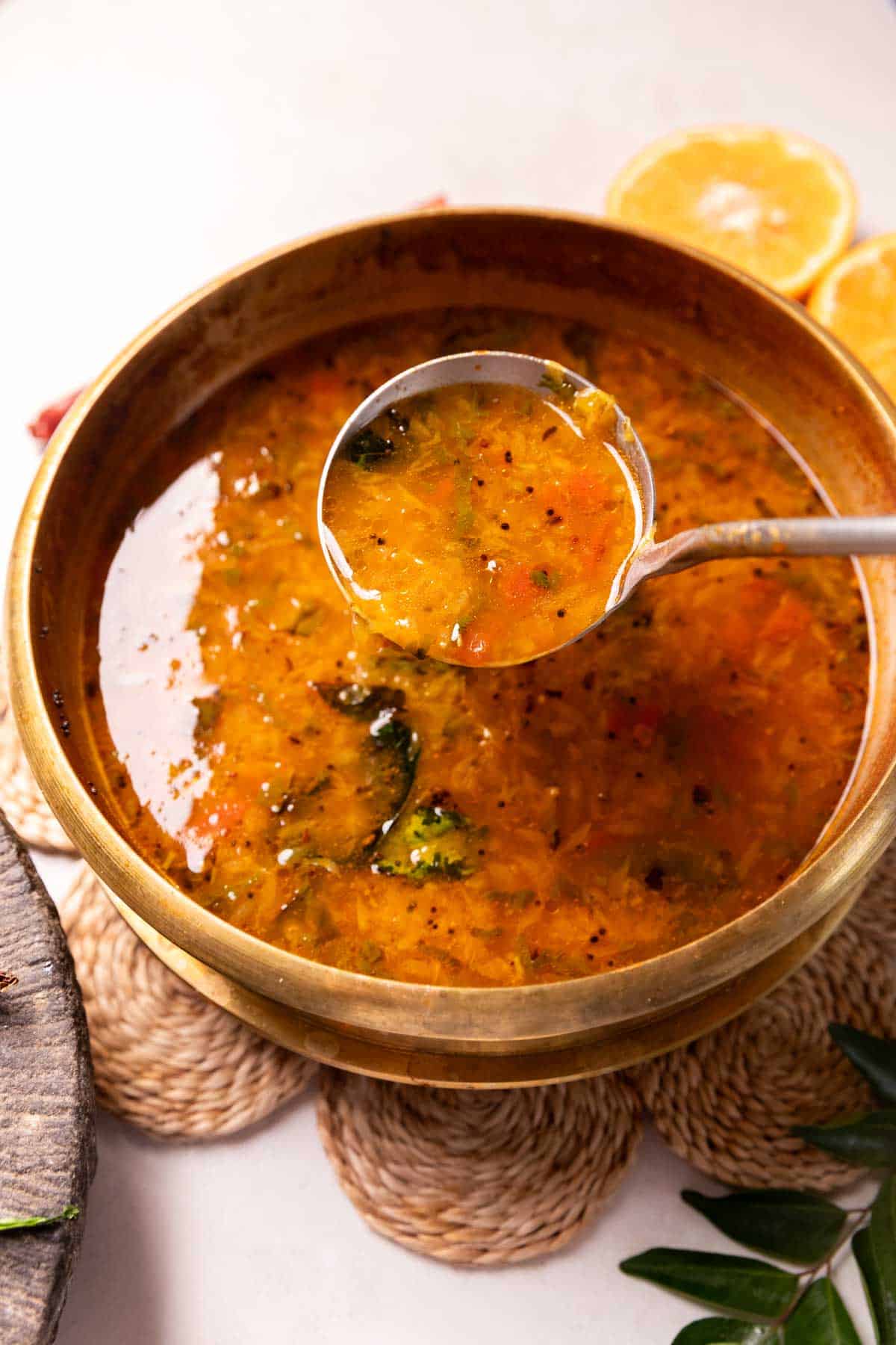 orange rasam in a container with a ladle 
