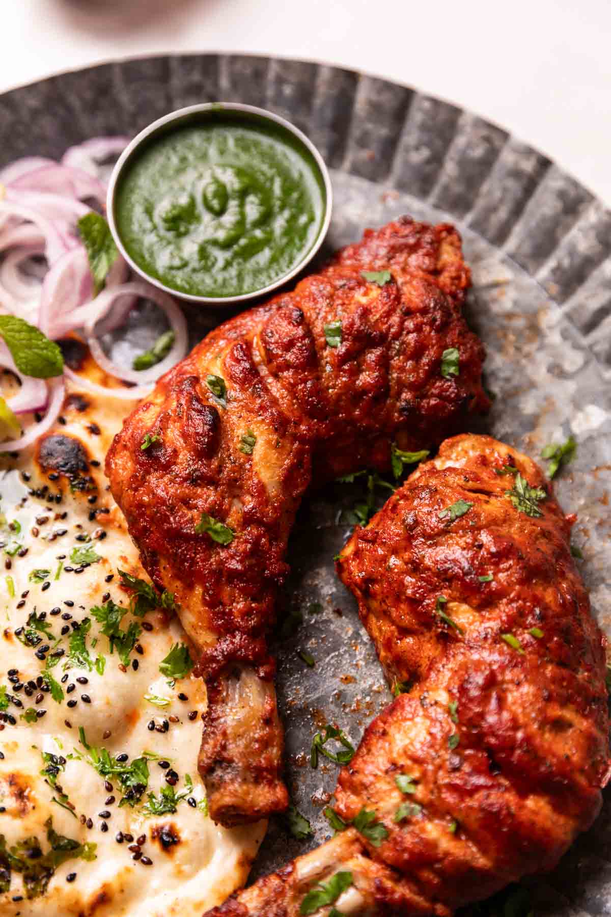 tandoori chicken served on a plate with naan, chutney, and sliced onions