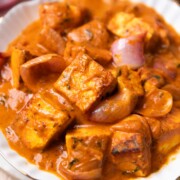 Paneer do pyaza served in a white bowl with accompaniments