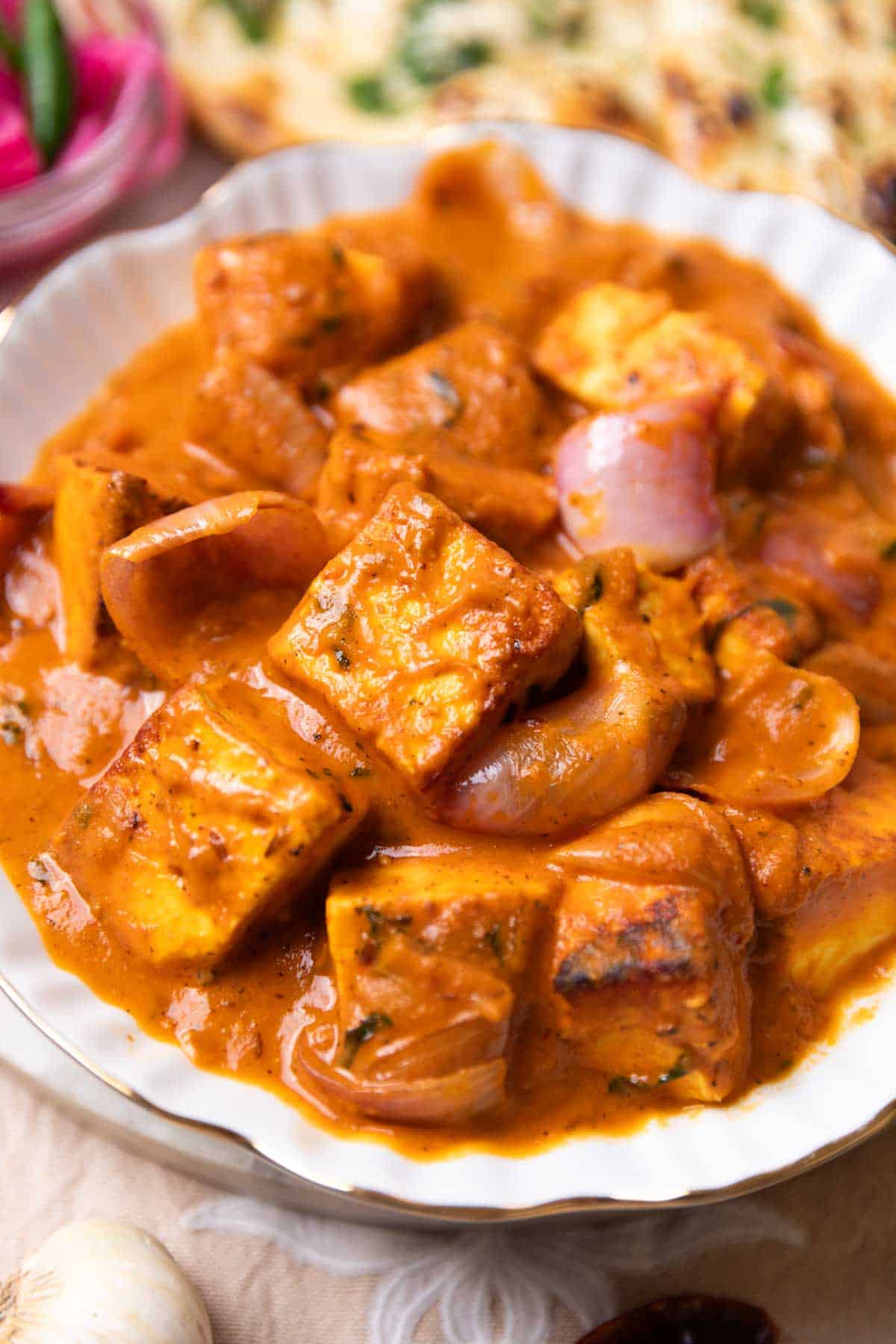 Paneer do pyaza served in a white bowl with accompaniments