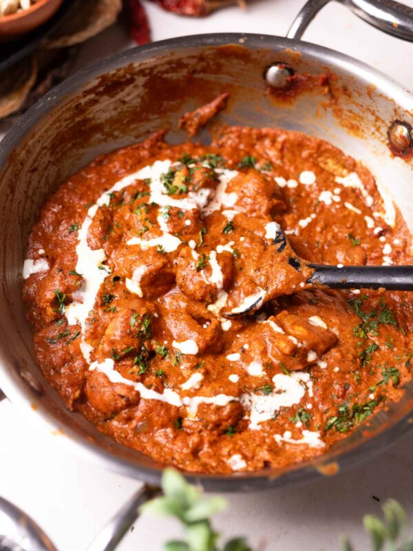 freshly made butter chicken garnished with fresh cream and herbs in a stainless steel kadai
