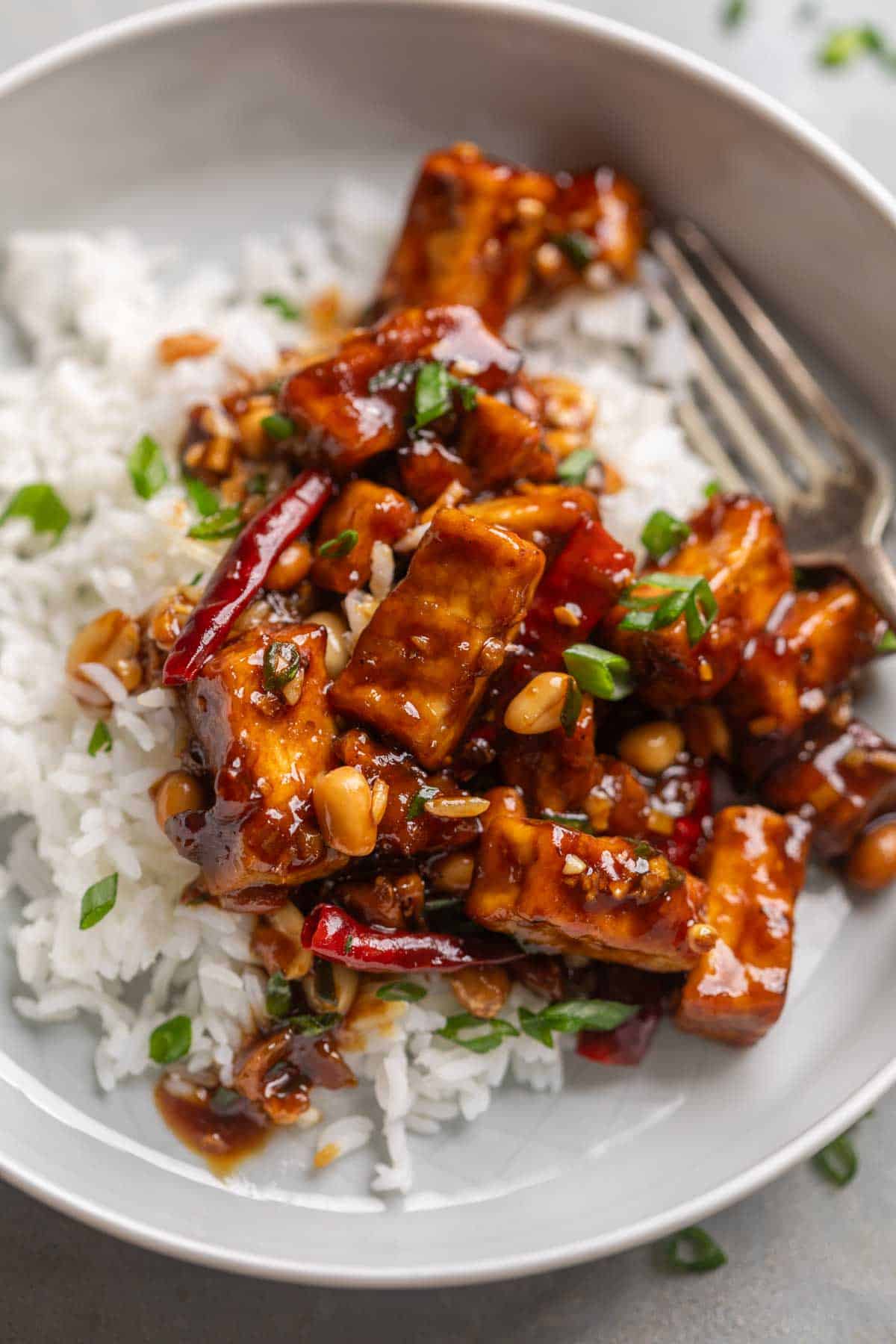 kung pao tofu served on a bed of steamed rice with a fork ready to be eaten