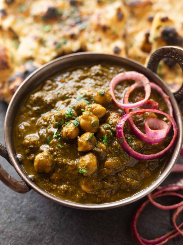 a bowl of chole palak served along with onion rounds and naan