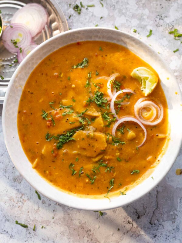 dal dhokli served in a bowl with onion rings and lemon wedges