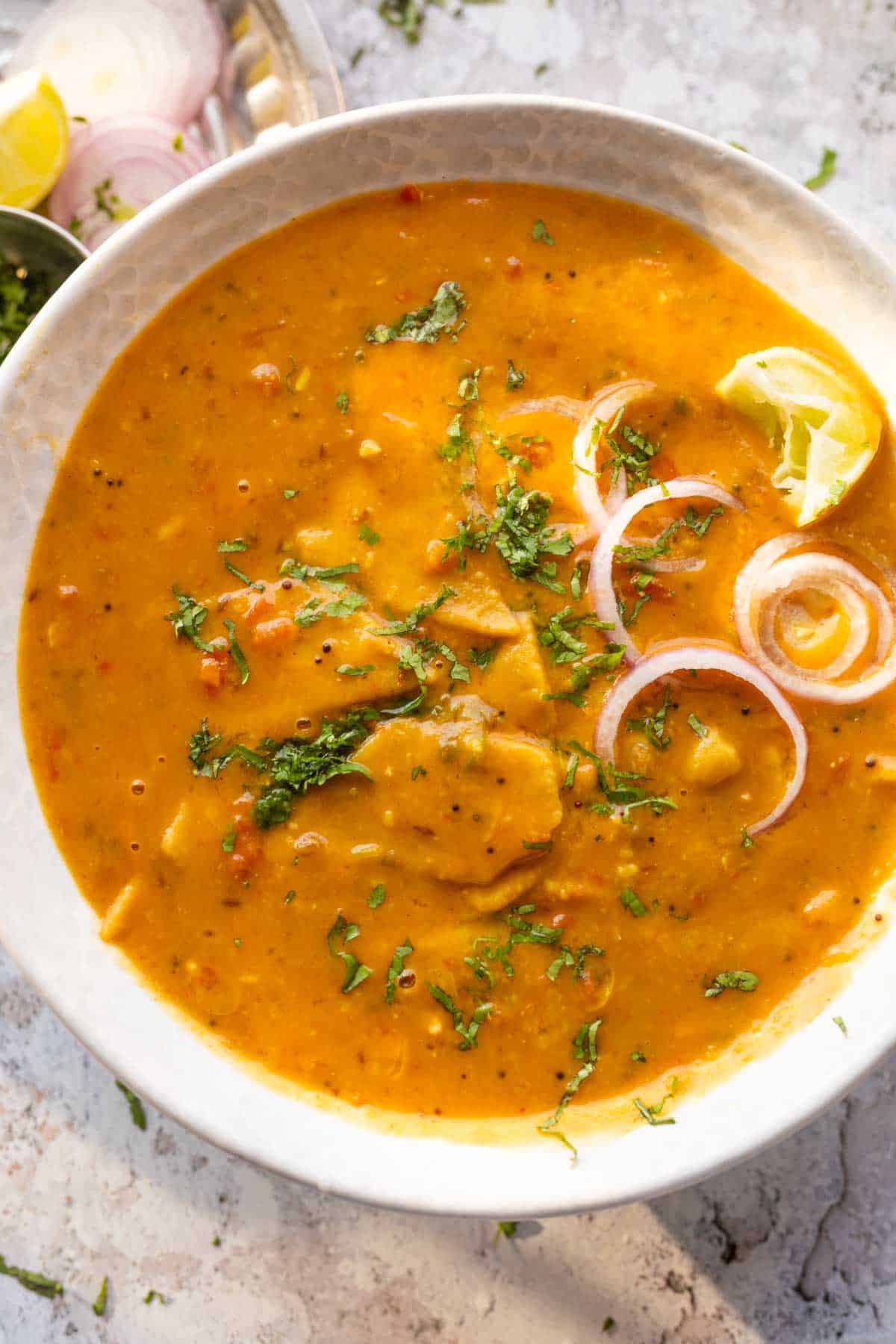 dal dhokli served in a bowl with onion rings and lemon wedges