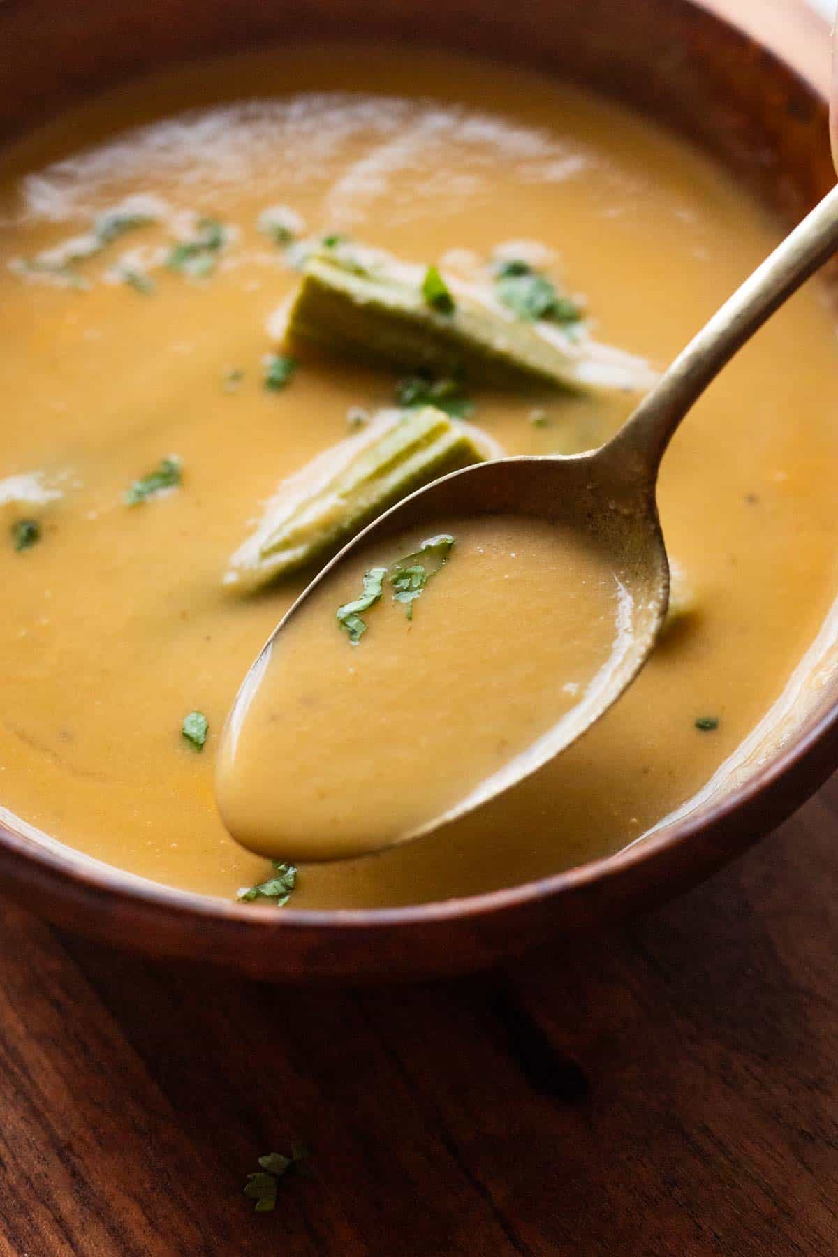 a close up image of drumstick soup garnished with boiled drumsticks and coriander leaves