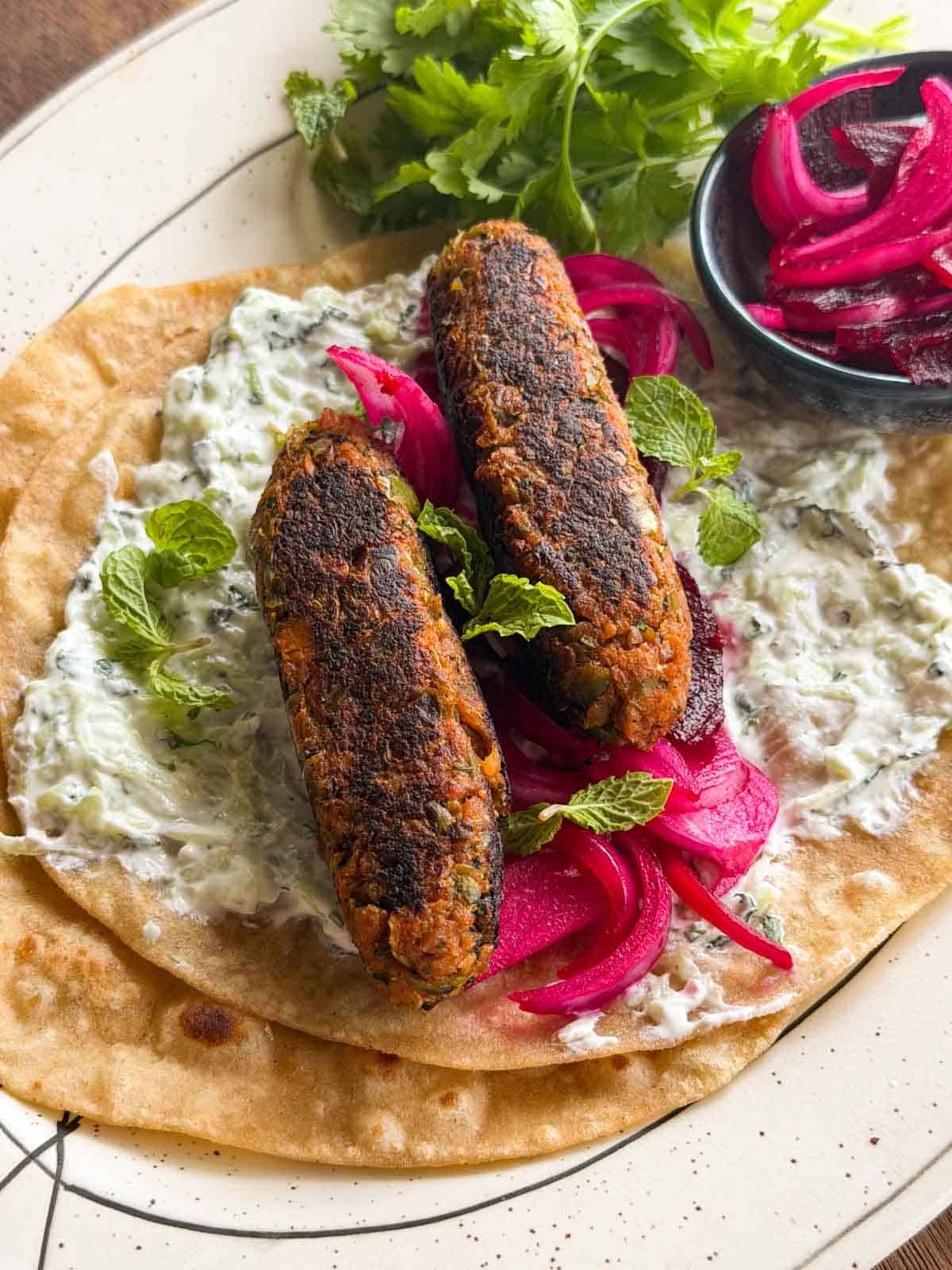 a close up image of veg seekh kebabs served on a roti with accompaniments